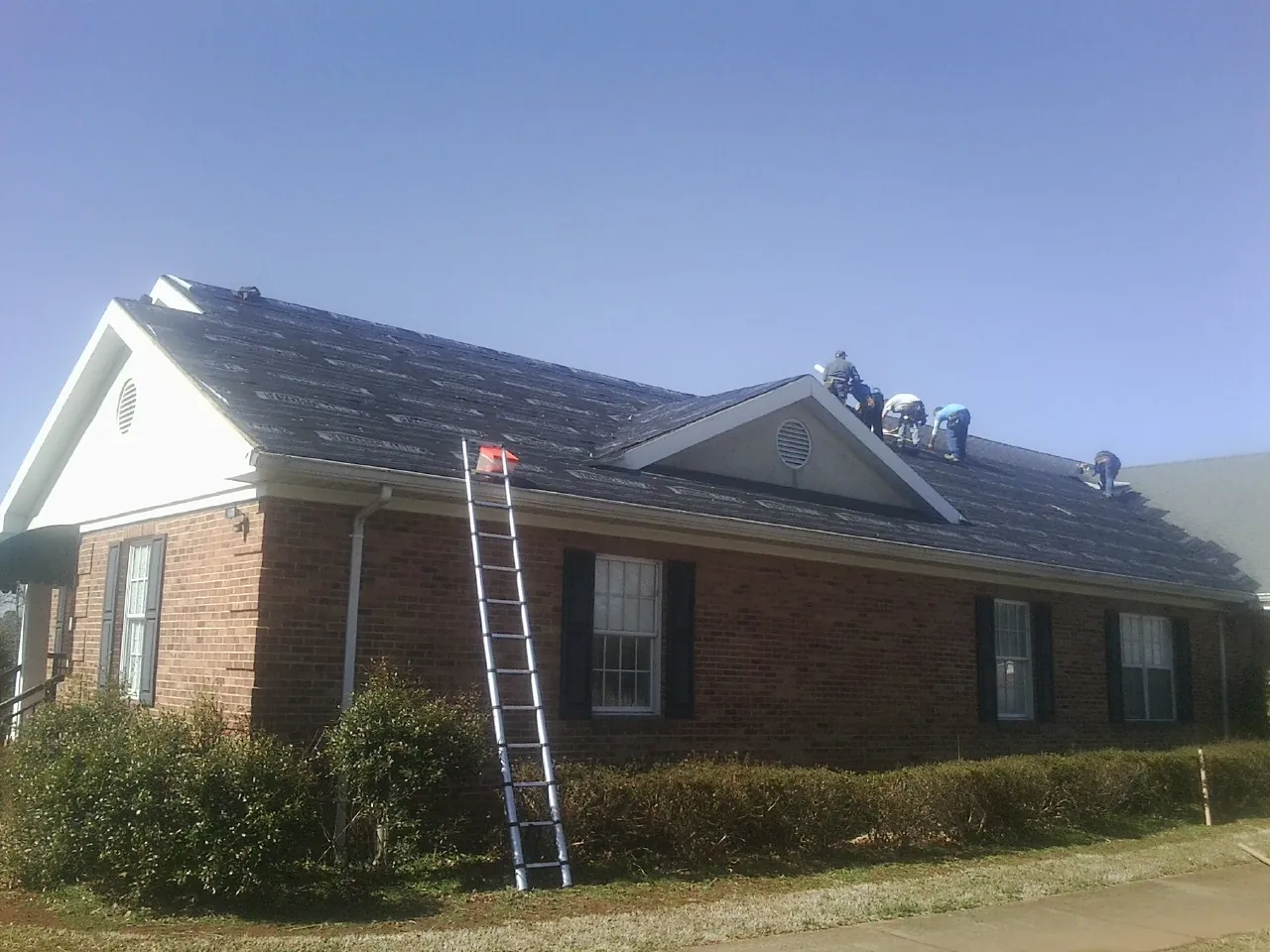 Crew tearing shingles off a brick ranch roof with a ladder set — Metal Roof Repair work by our crew in Rockport